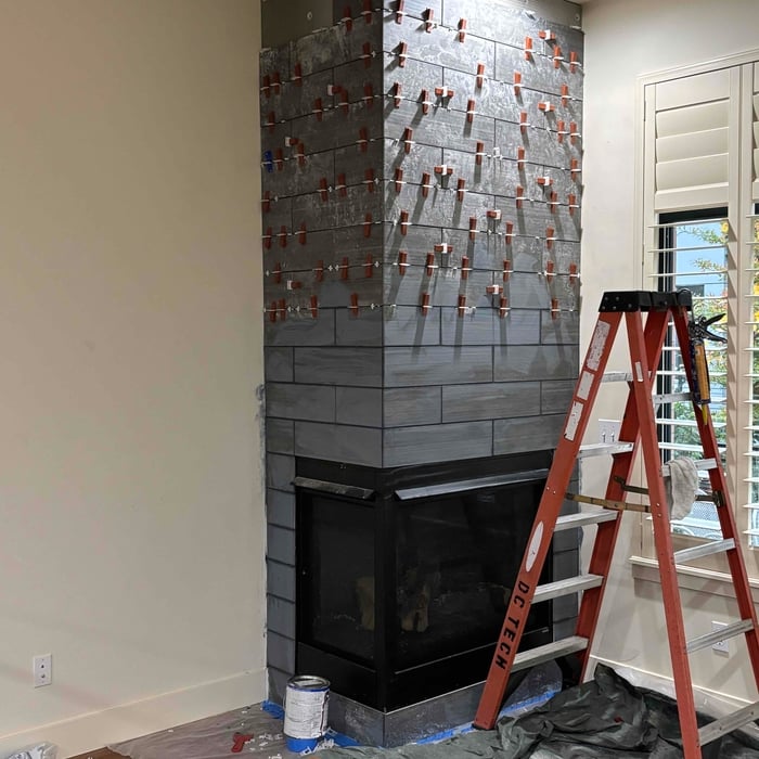 Tile fireplace surround mid-installation with leveling clips and a ladder on site
