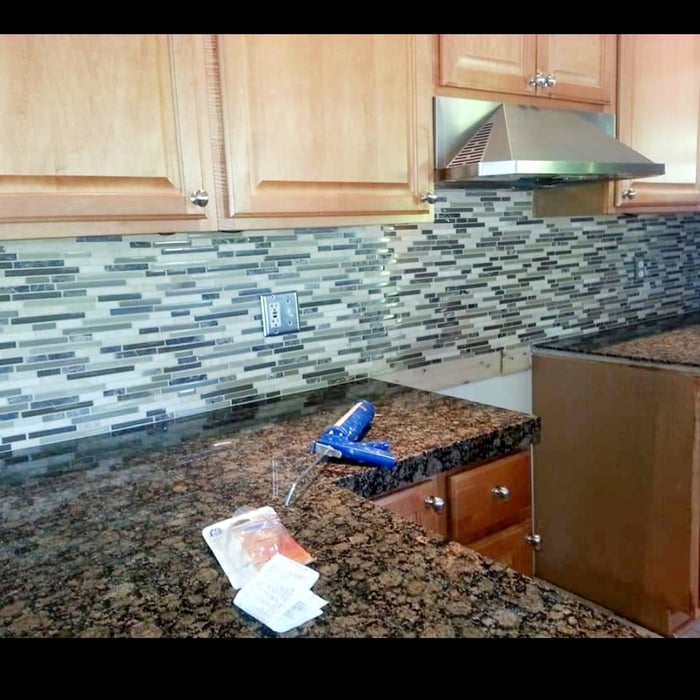 Glass mosaic tile backsplash being installed above granite counters in a maple kitchen