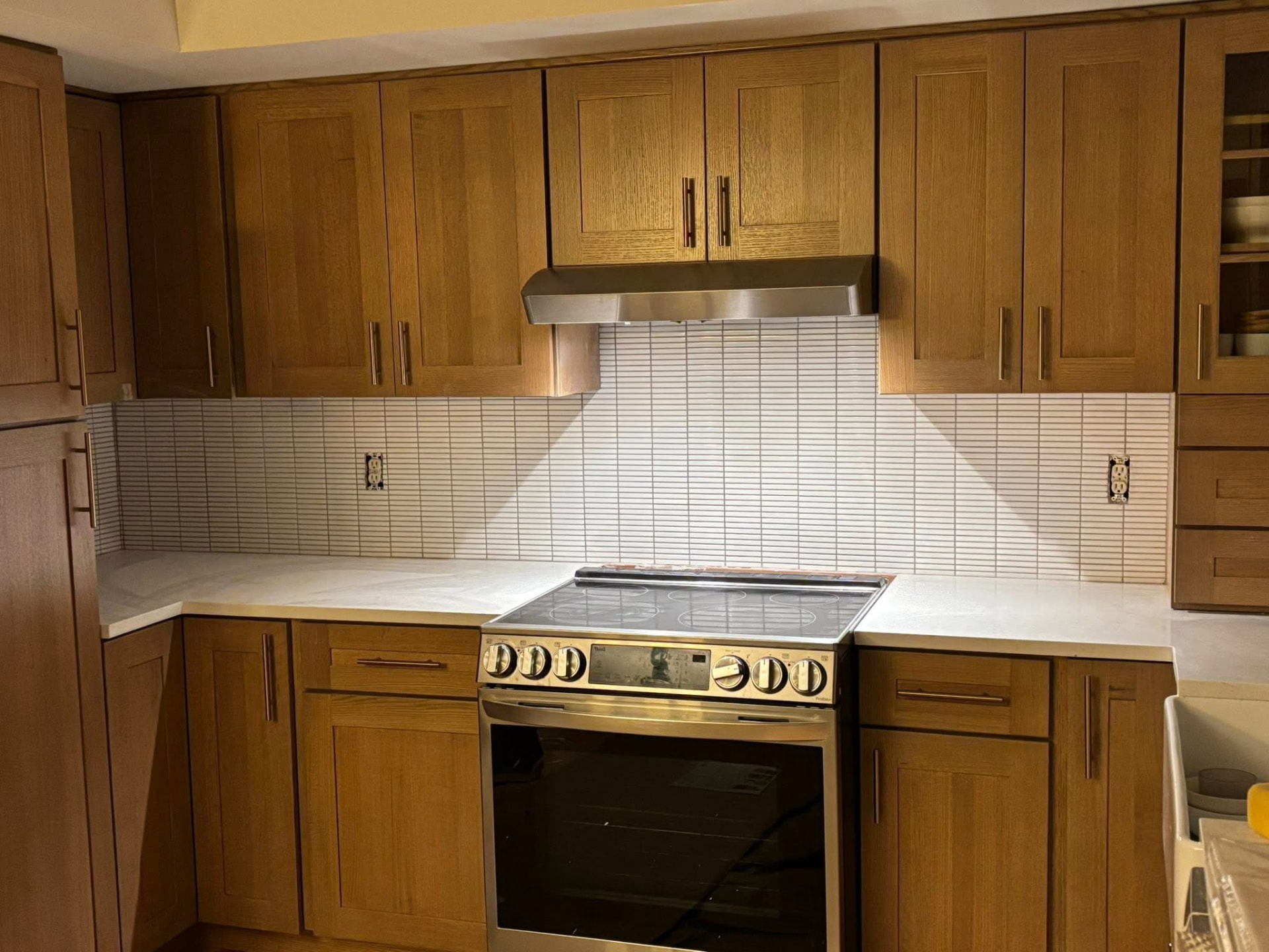 Kitchen with oak shaker cabinets, quartz countertop and a white stacked linear tile backsplash behind the range