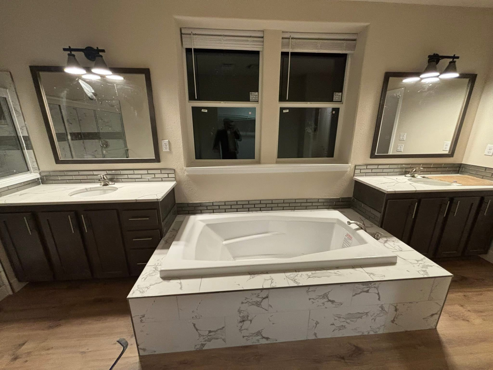 Bathroom with two dark wood vanities, quartz counters, framed mirrors and a tiled soaking tub