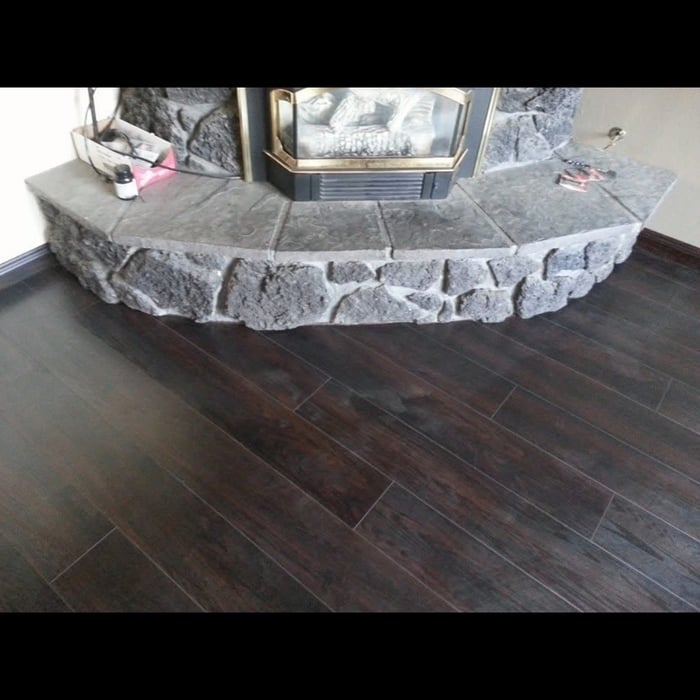 Stone-faced fireplace hearth with dark hardwood flooring scribed tight to the curved stone