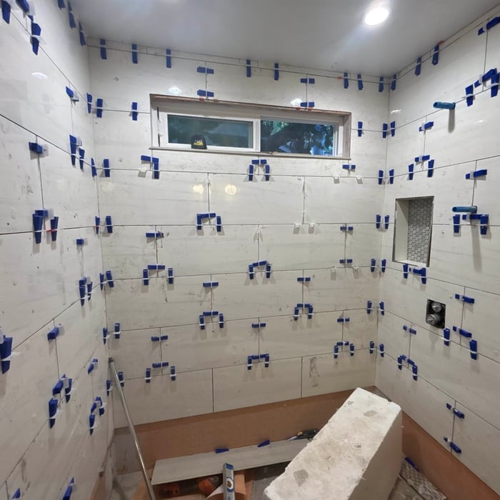 Shower walls mid-tile with leveling clips and spacers holding large-format tile flat