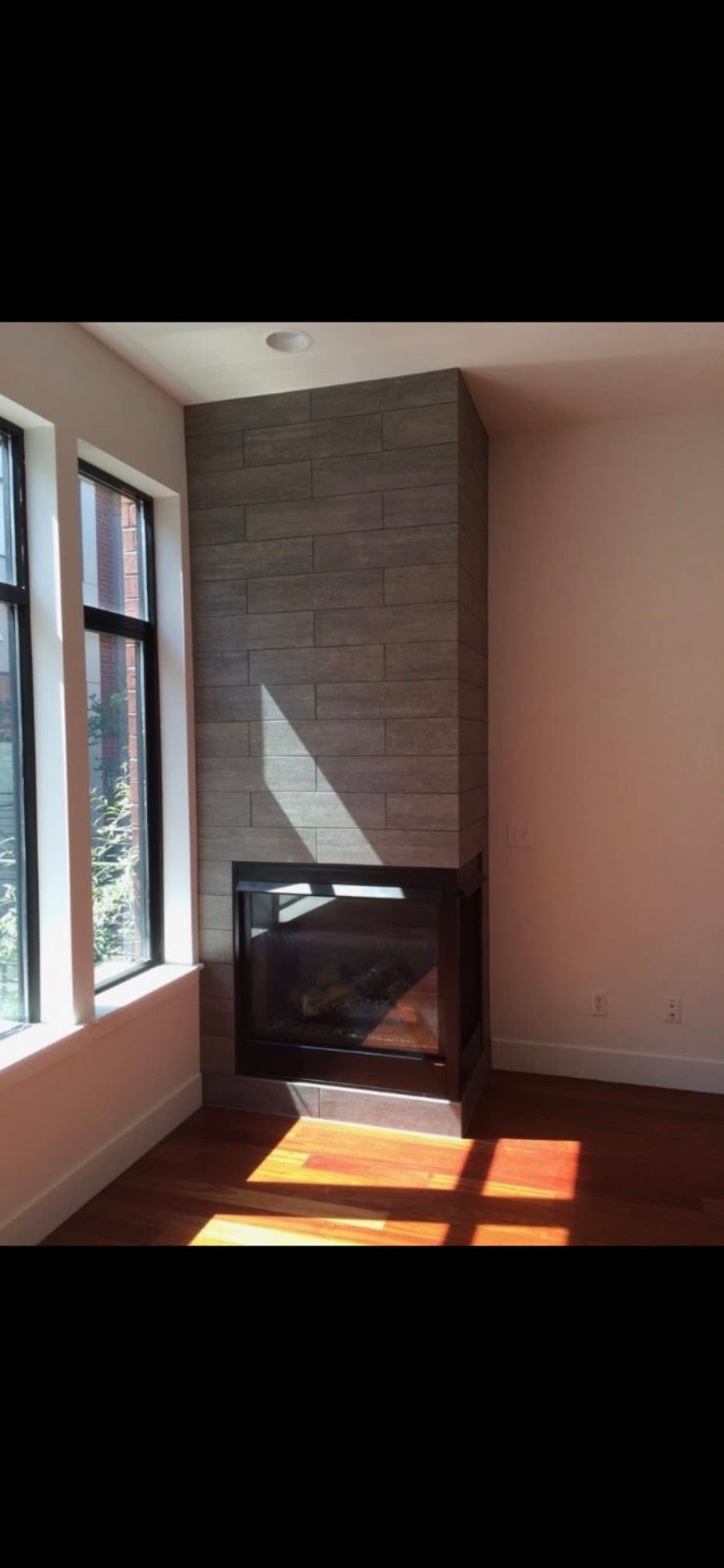 Floor-to-ceiling large-format tile corner fireplace surround in a bright room with hardwood floors