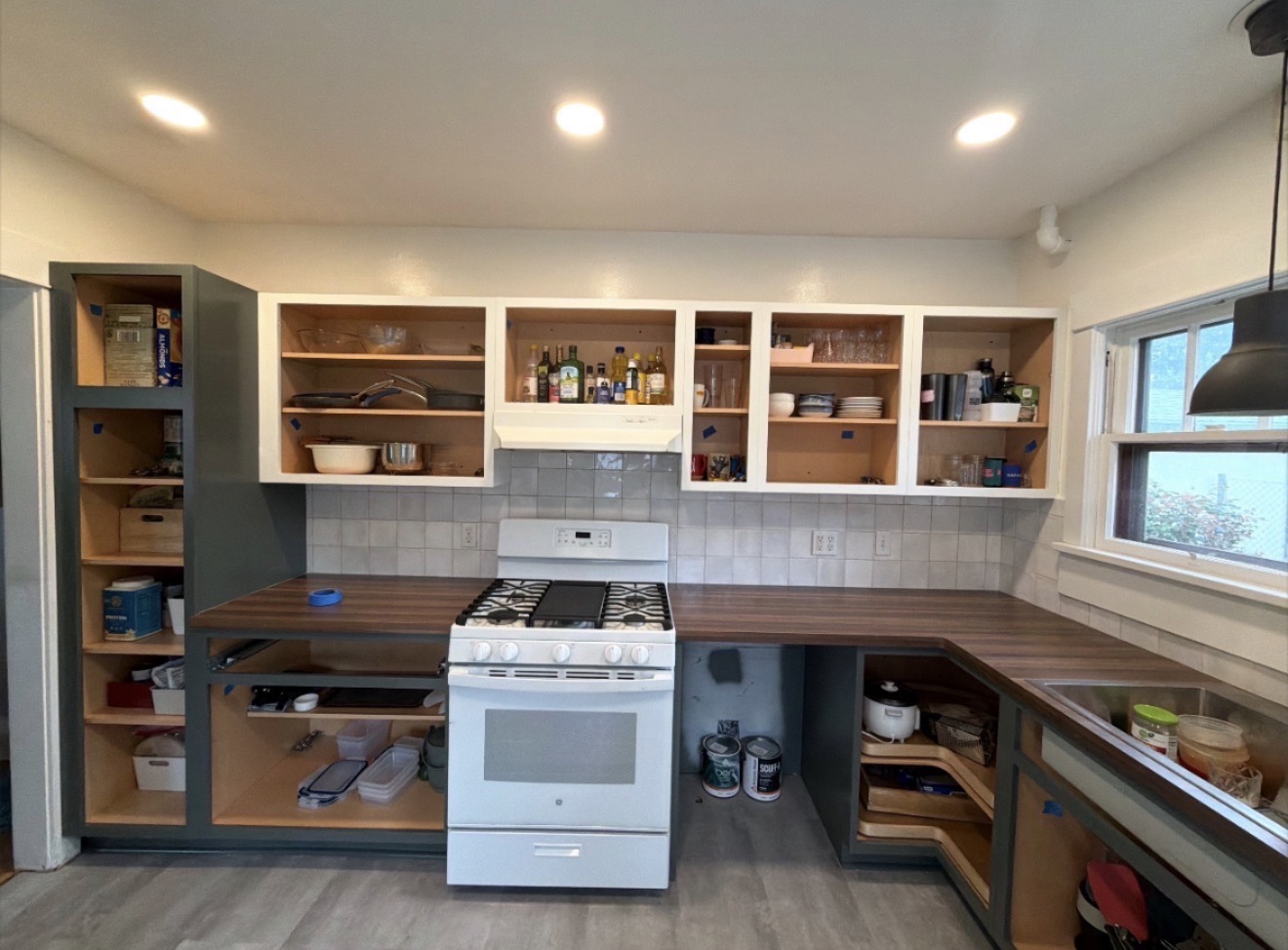 Kitchen mid-remodel with cabinet doors removed for refinishing, butcher-block counters and new plank flooring