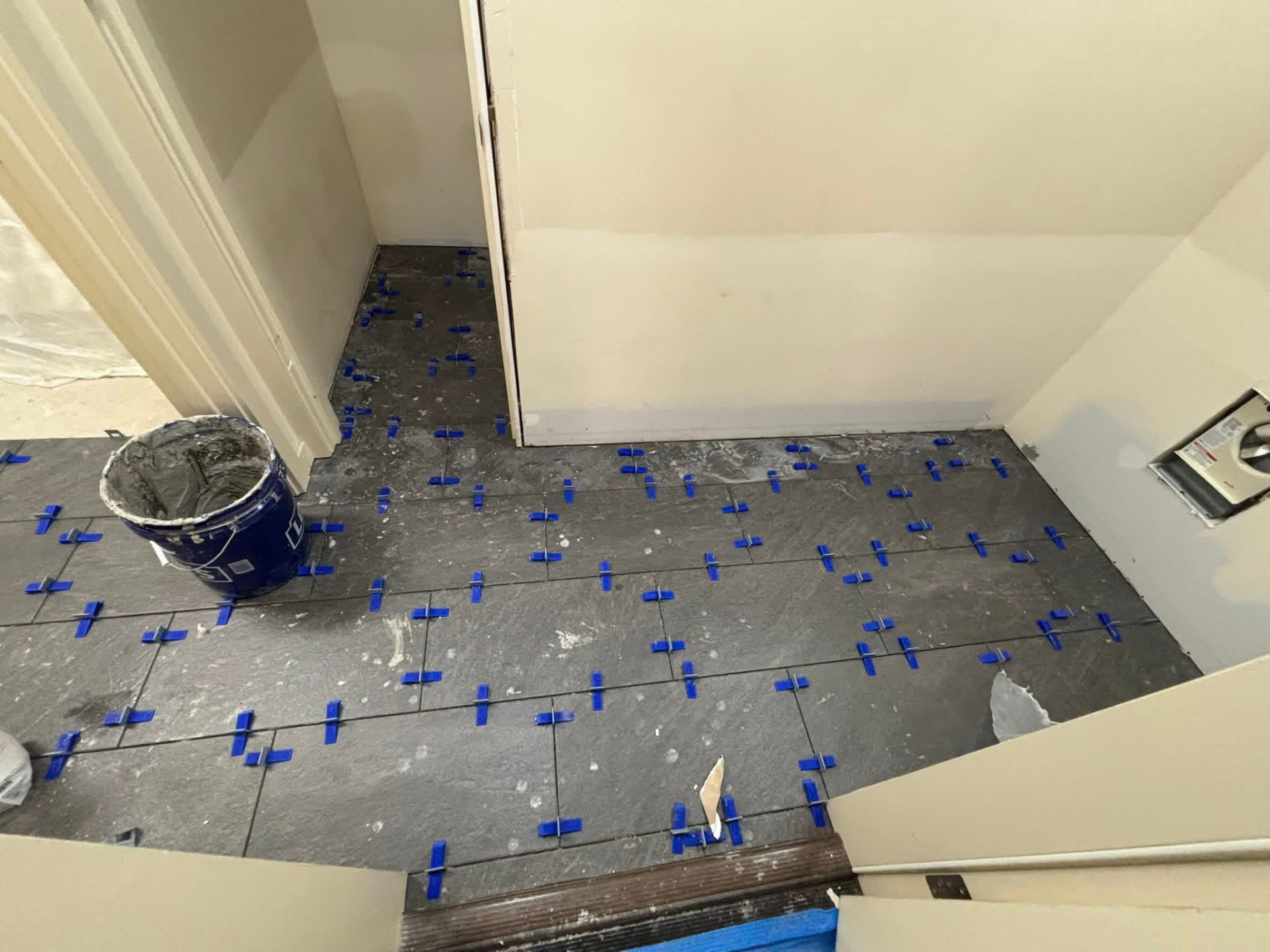 Slate-look floor tile mid-installation with blue leveling clips across the field