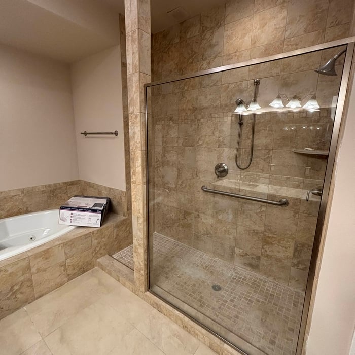 Travertine tiled bathroom with a glass walk-in shower, mosaic shower floor and a corner jetted tub