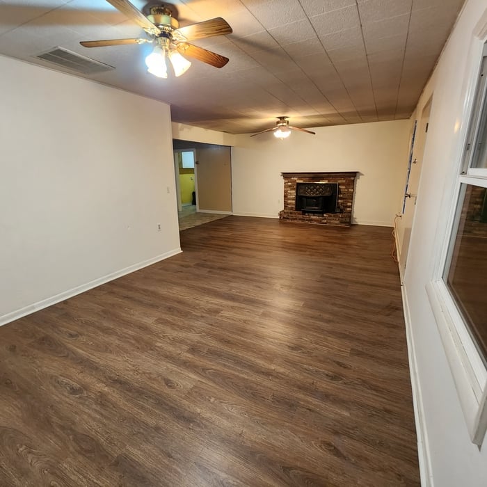 Restored living room with a brick fireplace, fresh paint and new wood-look plank flooring after a loss