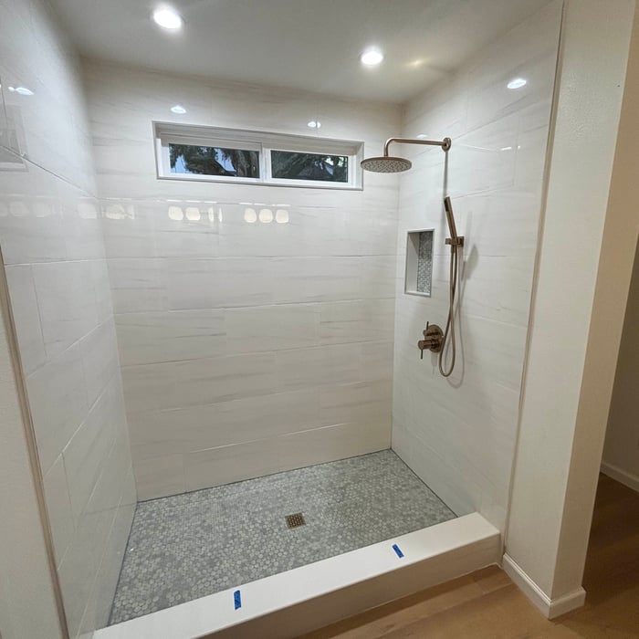 Walk-in shower with large white marble-look wall tile, hex mosaic floor and brushed brass fixtures
